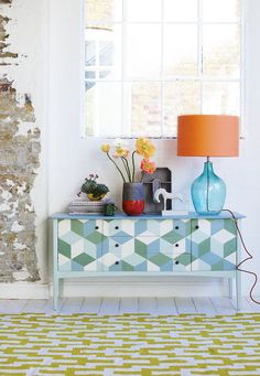 a blue and white dresser sitting next to a window with a lamp on top of it