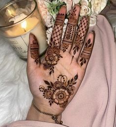 a woman's hand with henna on it next to a candle and flowers