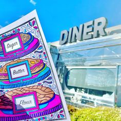 a person holding up a sign in front of a food truck with the word diner written on it