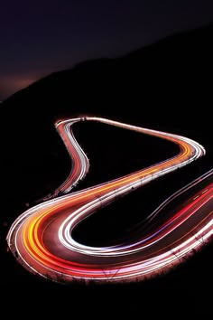 an aerial view of a highway at night with light streaks on the road and hills in the background