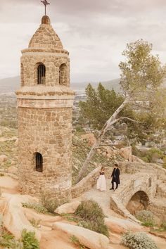 a bride and groom standing in front of an old stone tower with a cross on top