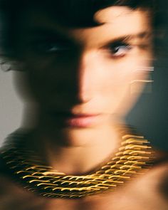 a close up of a person wearing a gold necklace and looking at the camera with blurry background