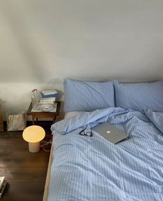 a laptop computer sitting on top of a bed next to a night stand and lamp