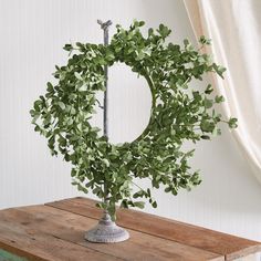 a green wreath sitting on top of a wooden table next to a white wall and window