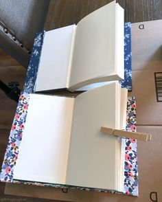 two open notebooks sitting on top of each other next to boxes and a pen