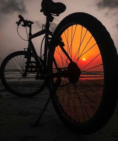 a bicycle parked on the beach at sunset with its tire in front of it, as the sun sets