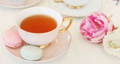 there is a cup of tea on the table with pink flowers and macaroons