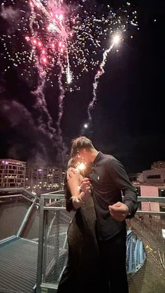 a man and woman kissing while fireworks go off in the sky