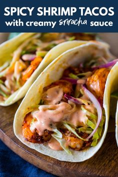 three tacos with meat, lettuce and sauce sitting on a wooden table