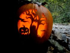 a carved pumpkin sitting on top of a pile of leaves next to a forest filled with trees