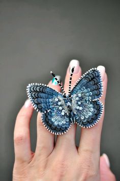 a woman's hand holding a blue and black butterfly brooch on her finger