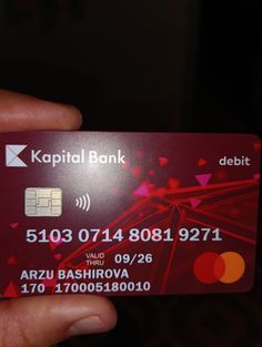 a person holding up a red credit card in their left hand with the words capital bank on it