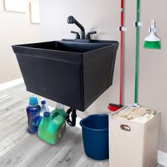 a black sink sitting next to two buckets and cleaning supplies on the floor in a bathroom