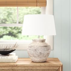 a white vase sitting on top of a wooden table next to a book and lamp