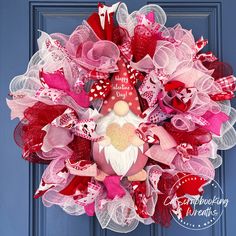 a pink and red mesh wreath with a gnome on it's face is hanging on a blue door