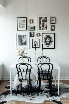 a dining room table with four chairs and pictures on the wall above it in black and white