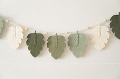 green and white leaves are hanging from a string on the wall in front of a white wall