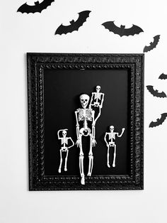 an image of halloween scene with skeleton family in black frame and bats on wall behind it