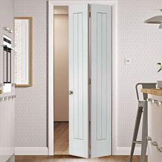 an open door leading to a kitchen with white walls and wood floors, in front of a wallpapered dining room