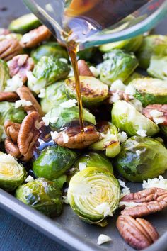 brussel sprouts with pecans, pecans and walnuts are being drizzled with maple syrup