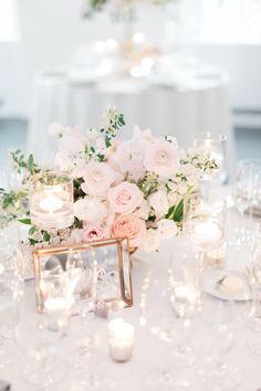 the centerpieces on this table are filled with white and pink flowers, candles, and greenery