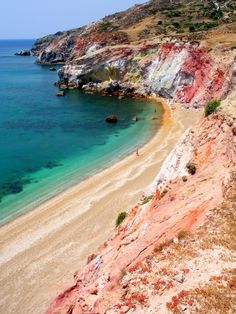 a sandy beach next to the ocean with clear blue water and cliffs on both sides