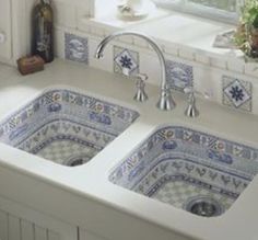 two blue and white tiles on the side of a sink in a kitchen with windows