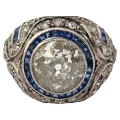 GIA certified Antique Art-Deco Diamond and Blue Sapphire Ring mounted in Platinum Art Deco engagement ring, sizzles in the center with a bright-white and sparkling European-cut diamond weighting approx. 2.05 to 2.10 carats (8.15mmX7.95X4.20mm); J/K color - SI clarity, the scintillating bezel-set stone is dramatically encircled with small seamlessly set blue calibre sapphires, and Fine piercing work, millegrain edging, and intricate hand-engraved decoration add the finishing flourish to this chic, sophisticated, and stunning Jazz Age jewel. ; Mounted, hallmarked and tested in platinum. Total diamond weight approx. 2.60 carats to 2.5 carats (2.cts and 0.65 cts) blue sapphire weight approx. 0.60 carats. Total weight :5.47g. Width in front 15mm. Ring Size: 58 (19 mm diameter ring size) (Mounte Blue Sapphire Ring, Ring Mountings, Jazz Age, Art Deco Engagement, Deco Engagement Ring, Art Deco Engagement Ring, European Cut Diamonds, Art Deco Diamond, Platinum Ring