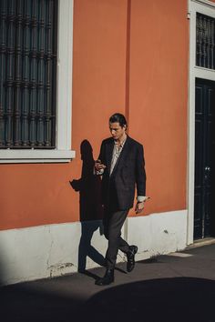 a man is walking down the street while looking at his cell phone in front of an orange building