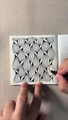 someone is drawing an intricate pattern on paper with black marker and pen, while another hand holds