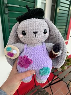 a crocheted stuffed animal is being held up by someone's hand in front of a green door