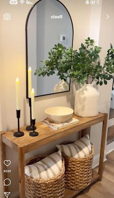 a wooden table topped with a mirror and two baskets filled with candles next to a plant