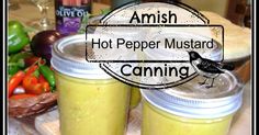 two jars filled with hot pepper mustard sitting on top of a table next to vegetables