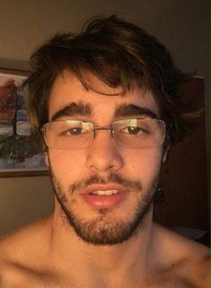 a man with glasses and no shirt is looking at the camera while he's taking a selfie