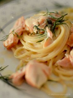 pasta with salmon and dill on top in a white plate, garnished with fresh herbs