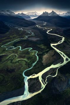 an aerial view of a river running through the middle of a mountain range with snow capped mountains in the background