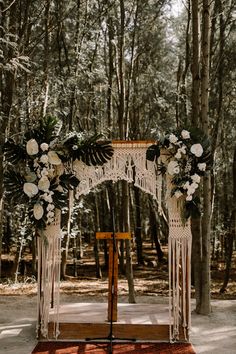 a wedding arch decorated with white flowers and greenery in the middle of a forest