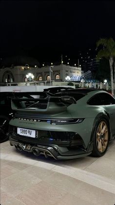 a green sports car parked in front of a building at night with its hood up