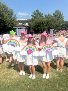 three girls in white dresses and pink hats holding rainbow signs