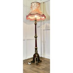 a lamp that is on top of a wooden floor next to a light fixture with a pink shade