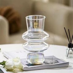 a clear glass vase sitting on top of a table next to a white rose and an open book