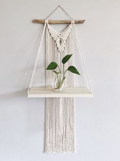 a white macrame wall hanging with a plant in a glass vase on it