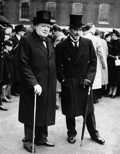 two men standing next to each other in front of a group of people wearing hats and coats