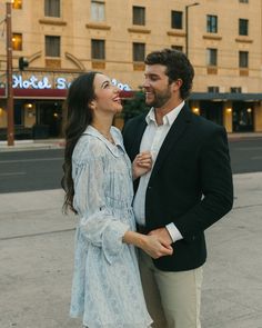 a man and woman standing next to each other in front of a building with a sign on it