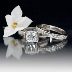 two wedding rings sitting next to each other with a flower in the background on a reflective surface