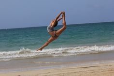 a woman doing a handstand on the beach with her feet in the air