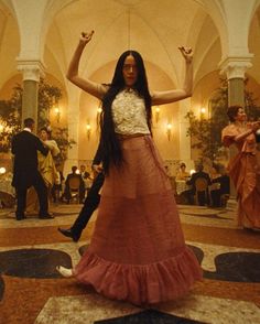 a woman in a long skirt is dancing with her arms up and legs spread out