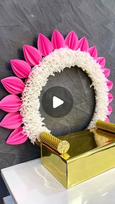 a large pink and white flower sitting on top of a gold box in front of a gray wall