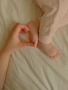 a person holding the foot of a baby on top of a white bedding sheet