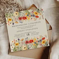 a wedding card with flowers on it sitting on top of a bed next to some dried plants